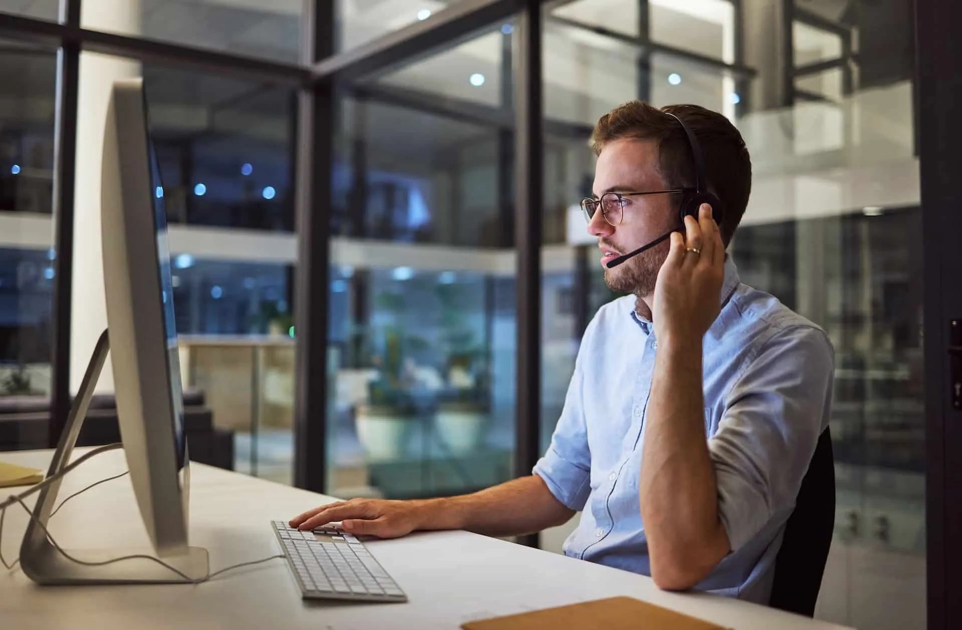 Mitarbeiter mit Headset am Bildschirm im abendlichen Büro – der Schutz läuft weiter, auch außerhalb der Bürozeiten